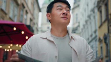 Close-up chinese male tourist walking on street exploring city landmark using paper map looks around happy young man student looking for right way in travel guides search location explore new locality