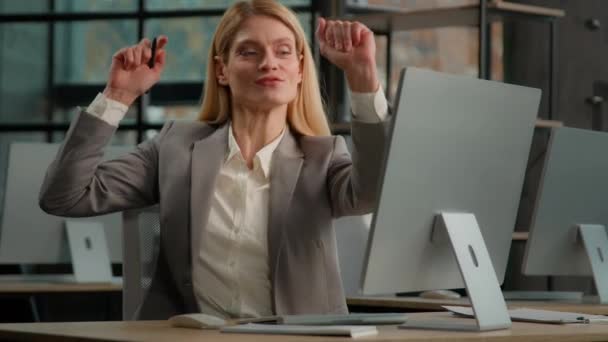 白种人中年女性在工作场所跳舞 听着音乐 像麦克风一样唱歌 商界女企业家办公室里的女企业家在电脑音频中欢唱着滑稽的舞曲 — 图库视频影像