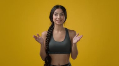 Indian woman lady trainer coach yoga teacher athlete sporty fitness girl in yellow studio talk to camera explain show exercise for hands biceps flexibility stretching arms talking sport blog workout