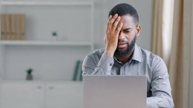 Stressed disappointed African American ethnic bearded man holding head with headache tired overworked manager reading bad news office worker businessman with laptop computer failure online problem