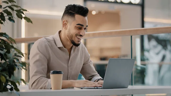 Indian Hispanic ethnic businessman male worker guy man in cafe with laptop happy with luck fortune internet betting victory celebrate bet online lottery game winning victory business success achieve