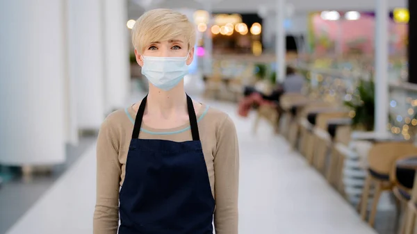 Mature adult middle aged 40s woman in medical mask restaurant cafe worker looking at camera crossing arms female waitress saleswoman in apron working in quarantine pandemic coronavirus small. High