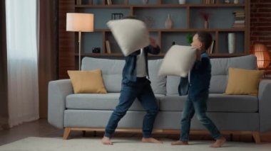 Happy two energetic little preschool kids siblings brothers African American ethnic children friends at home living room having fun cheerful laughing playing funny fighting pillows fight battle game