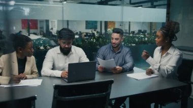 View from behind glass African American female team leader company CEO check strategy with diverse colleagues paperwork documents multiracial business people work project together at office teamwork