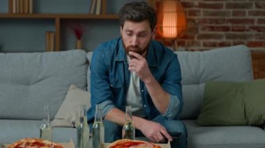 Portrait of upset adult man single caucasian male looking at pizza and beer sad unhappy guy lonely celebrate alone at home sit on couch no guests on birthday party feeling abandoned quarantine concept