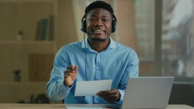Skilled salesman african man businessman business consultant in headphones talk video conference online call on laptop communicating by webcam male teacher manager instruct distant use paper documents