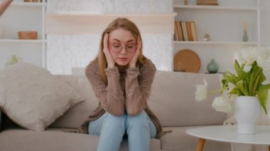 Tired upset Caucasian mother sitting on sofa at home sad frustrated stressed exhausted fatigued mom suffer headache with active noise difficult kid child baby girl daughter running around playing