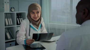 Female doctor woman in hijab neurologist radiologist analyze MRI scan x-ray diagnostic result make professional radiology expertise check trauma on image talk with male patient on medical consultation