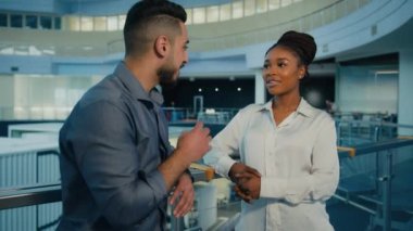 Friendly diverse multiethnic business partners colleagues talking in office hall. African American woman businesswoman and Indian Arabian man businessman talk corporate discussion conversation at work