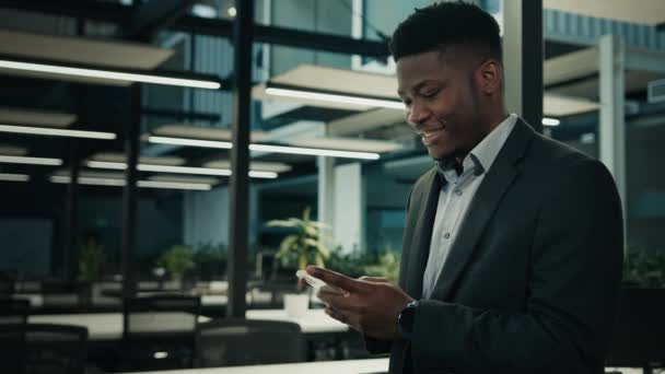 ハッピー千年アフリカ系アメリカ人男性ビジネスマン男性従業員チャットオンライン携帯電話遠くのウェブネットワーキング使用電話インターネットブラウジングモバイルアプリスマートフォン画面で見る読み取りメッセージ — ストック動画