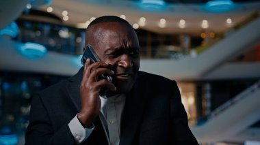Angry senior ethnic man executive businessman thinking answer displeased mobile call African American angry talking mobile phone indoors stressed middle-aged male man conflict problem talk furious