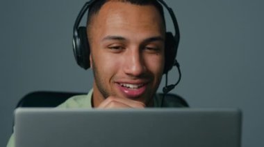 Close-up young latin american man on gray background talking video call on laptop using headset friendly businessman consultant call center operator work in helpline advise client at online conference