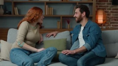 Caucasian hispanic couple adults man talking with woman sit on couch in living room ethnic diverse friends spouses family chatting friendly talk indoors female male discussing share news plans at home