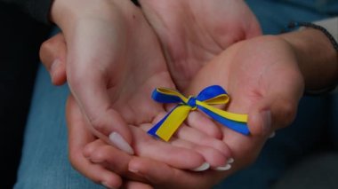 Close-up woman and man hands of multiracial family couple husband wife holding yellow blue colors ribbon national symbol Ukraine female male palms together support ukrainian people concept of charity
