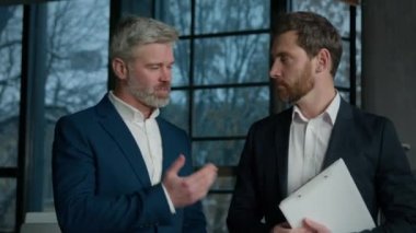 Two caucasian businessmen talking walking in office business partners colleagues discussing new project mature man manager consultant sales agent explaining benefits contract to young male client