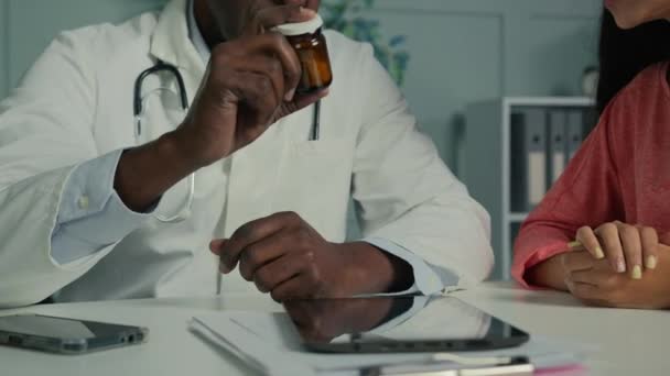 医師療法士アフリカ系アメリカ人男性シニア男性は若い患者の女性にボトル薬を与えます薬抗生物質ビタミン錠病気の女性のクライアントは 薬の治療を取る — ストック動画
