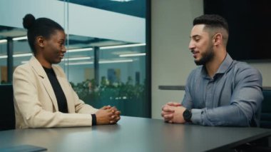 Indian Arabian executive employer HR manager salesman leader company CEO man businessman talking with African American candidate woman businesswoman in office shake hand handshaking hiring agreement
