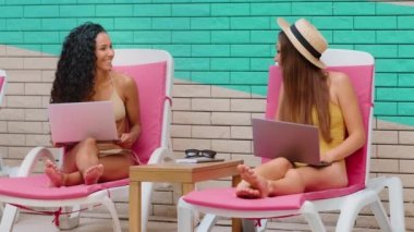 Female Caucasian Latina friends businesswomen bloggers young 20s multiracial women tourists students relaxing near poolside working laptop remote job in summer holidays booking hotel travel business