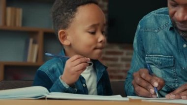 African American child boy with ethnic father learning at home. Dad teacher helping little son pupil preparing for test primary school kid doing homework with daddy man writing task distant education