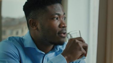 African american healthy man drinking water glass of cold fresh drink sit at home office feel thirsty hydrate body health care habbit keep aqua balance dreaming ethnic businessman looking at window