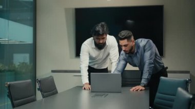 Two Arabian Indian workers managers partners businessmen in office discuss business problem with laptop analyze online result African American woman leader walk in boardroom help with computer work