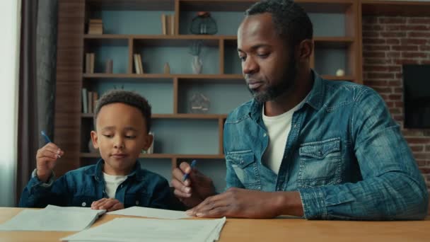 アフリカ系アメリカ人の父は 小さな息子の書き込みヘルプを教える子供の男の子と一緒にテストレッスンクラスのお父さんを書きます宿題をする子供と一緒に子供を助ける家庭学習ホームスクール — ストック動画
