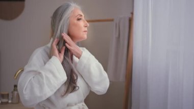 Disease hair lose problem. Caucasian old senior mature 60s woman 50s lady in bathroom checking hairdo sad about dry bad hairstyle need moisturizing procedure alopecia sickness anxiety baldness balding
