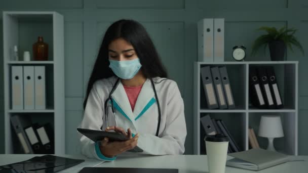 Webカメラビュー若いアラビア民族の女性医師の顔のマスクは デジタルタブレット検索ウェブ上のヘルスケアアプリを使用してビデオチャット仮想オンライン協議を呼び出します医療情報現代の技術遠隔医療 — ストック動画