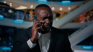 Pensive senior ethnic man executive businessman thinking answer displeased mobile call African American angry talking mobile phone indoors stressed middle-aged male man conflict problem talk furious