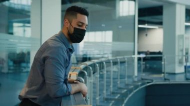 Side view Indian Arabian ethnic multiracial man executive employer entrepreneur corporate worker male boss leader businessman company CEO wearing medical face mask looking away in office hall thinking