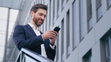 Smiling happy handsome caucasian man holding mobile phone checking email reading message receiving good news successful businessman browsing social network makes order in online store using cellphone