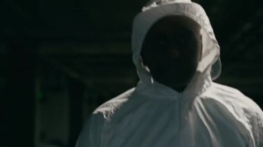 Serious african american man in overalls walking in dark basement close-up male doctor medical worker scientist lifeguard in special chemical white suit uniform and protective mask fighting pandemic