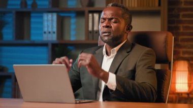 Tired african american man typing on laptop working at home office exhausted businessman feeling headache rub temples suffer from symptom chronic migraine feel fatigue from overwork have painful head
