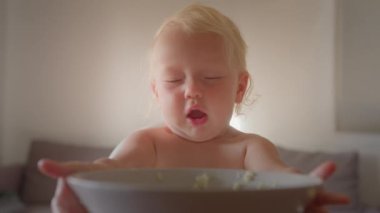 Caucasian baby girl infant sit on feeding high chair put plate eat milk porridge with hands at home kitchen or nursery kindergarten happy newborn child with food stained face little boy eating food