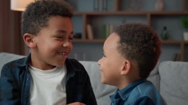 Two little boys friendly talking laughing at home. Ethnic African American multiracial multiethnic male kids schoolboys pupils sons indoors talk laugh together. Children brothers friends conversation