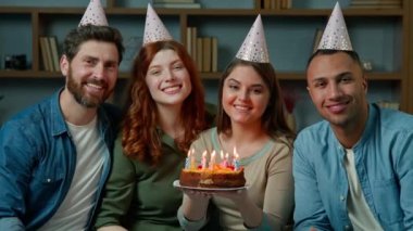 Friends in party caps celebrate festive event at home diverse multiracial people men women hold birthday cake with candles. Group portrait smiling african american caucasian hispanic ethnicity family