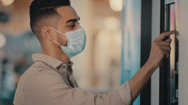 Side view male passenger Indian Hispanic man in medical mask in airport terminal businessman in bank office using self-service machine online payment with auto tech touch screen panel terminal display