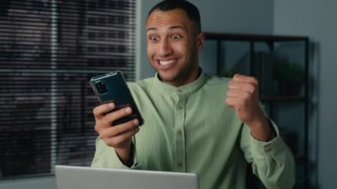 Excited african american businessman receiving email reading good news on mobile phone overjoyed man winner entrepreneur sitting in office celebrating online victory enjoy success winning on internet