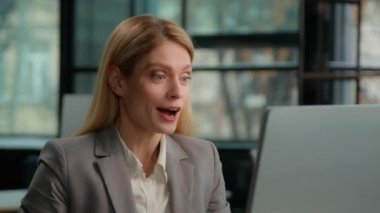 Office female worker Caucasian middle-aged smiling businesswoman sitting at desk working on computer celebrate online business success adult 40s woman entrepreneur happy laptop winning good news win