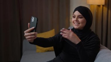 Islamic muslim woman 20s girl use mobile phone webcam conference app talking online chatting. Female blogger speaking indoors arabian lady businesswoman in hijab recording selfie video on smartphone