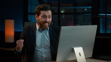 Overjoyed Caucasian male businessman winner employee boss investor office worker sit at desk work with computer win online bet internet victory happy adult man achieve good result celebrating success