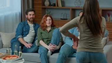 Creative ethnic four adults friends play game intellectual activity at home diverse people watch at expressive woman performance gaming task. Multiracial men and women guessing ask questions laughing