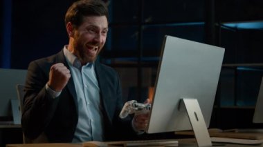 Caucasian winner businessman adult happy man employee gamer play console at office hold controller joystick playing video game on computer in evening win gaming level. Scared male start online work