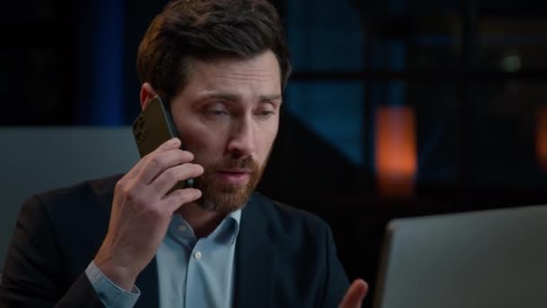 閉じる大人中高年の白人ビジネスマンの男はオフィスの机に座って携帯電話を話しているコンピュータを見て屋内男性投資家の上司とチャット電話ビジネスマルチタスク作業 — ストック動画