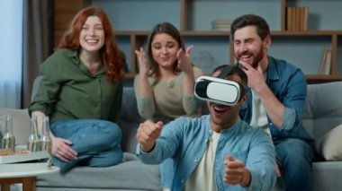 Gaming group multiracial ethnic diverse friends women men on couch support african american man gamer playing virtual reality game level in VR glasses AR headset metaverse simulator fun entertainment
