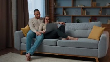 Ethnic multiracial family husband wife cuddle on cozy sofa shopping online at home use laptop computer watch film together adult couple african american man caucasian woman browsing internet website
