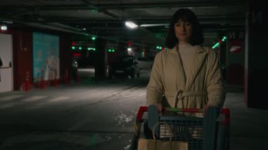 Young woman housewife businesswoman female lady girl with shopping trolley supermarket cart walking at market mall parking lot walk to car automobile with bags purchases after buying with discounts