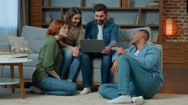 Multiracial team friends ethnicity diversity shoppers sit in living room work with laptop use credit card for online payment ordering delivery service spending money finances internet shopping talking