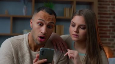 Multiethnic african american man caucasian woman happy couple use mobile phone device look at cellphone screen read good news approved bank loan mortgage win bonus on smartphone online victory fortune