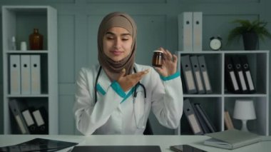 Female doctor arabian woman pharmacist use video conference app consult patient online recommend medical bottle with pills vitamins painkiller tablets pharmaceutical promotion of new health medication